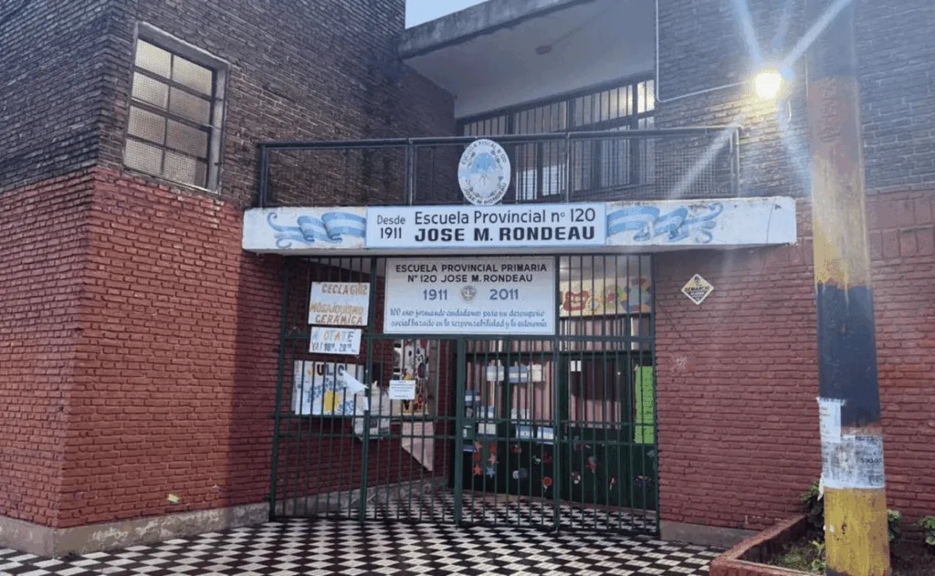 Escuela secundaria en Rosario con patrullero policial en la puerta y alumnos saliendo