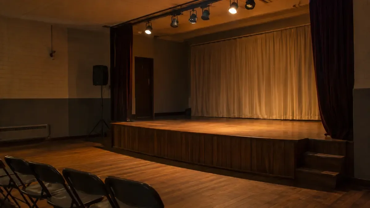 Un escenario vacío con luces cálidas en un centro comunitario, plano medio documental, perspectiva natural