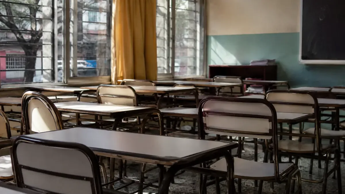 Pupitres ordenados en un aula sin estudiantes en una calle urbana argentina, vista en tres cuartos, profundidad de campo suave