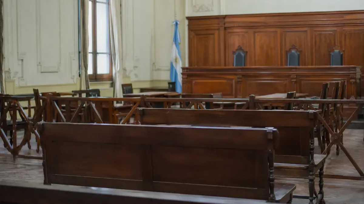 Una sala de audiencias vacía con bancos de madera en una calle urbana argentina, vista en tres cuartos, profundidad de campo suave