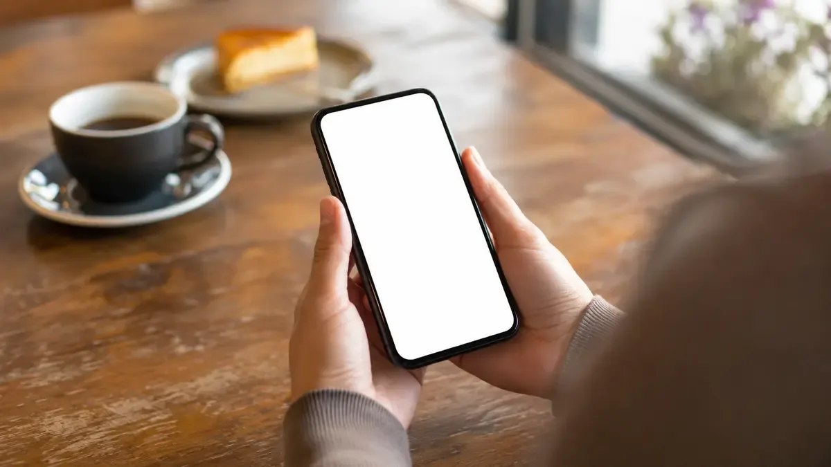 Manos sosteniendo un teléfono celular con la pantalla encendida sobre una mesa