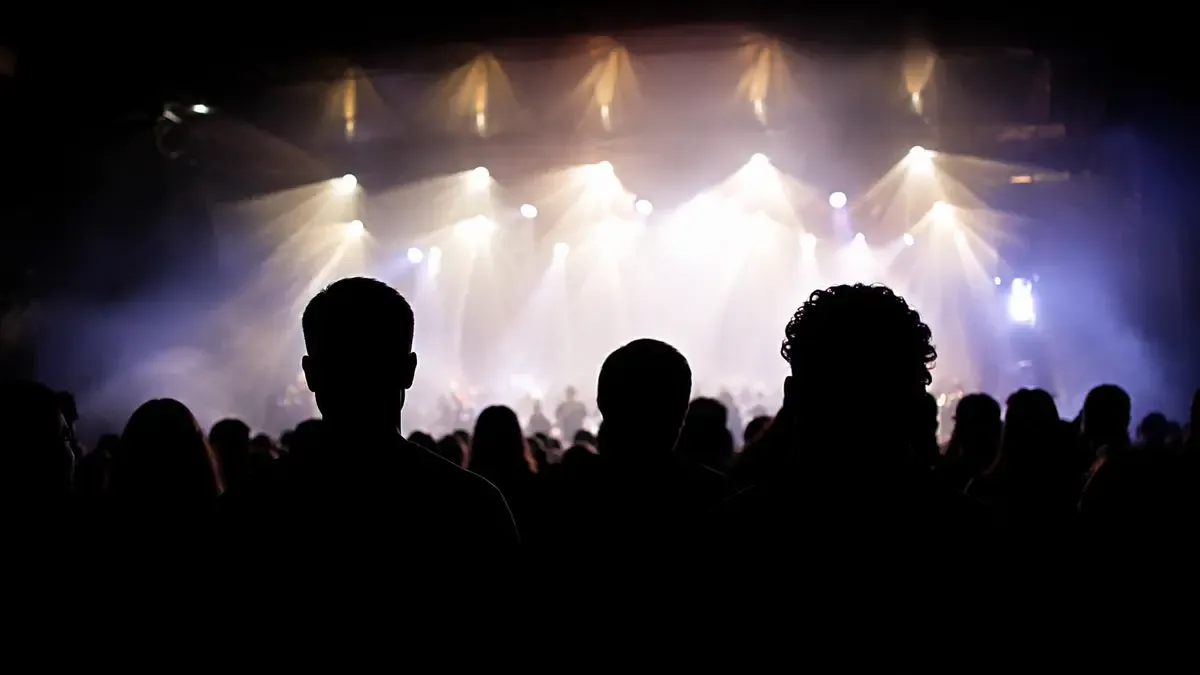 Siluetas de público en contraluz frente a un escenario iluminado