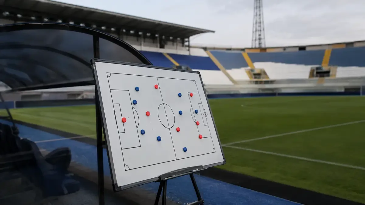 Una pizarra de cancha sin letras junto a fichas magnéticas en un estadio local vacío, vista en tres cuartos, profundidad de campo suave