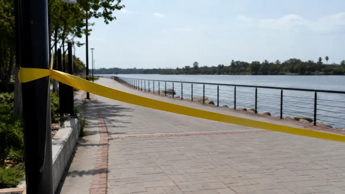 Cinta de seguridad lisa delimitando una vereda vacía en un paseo costero junto al río, plano medio documental, perspectiva natural