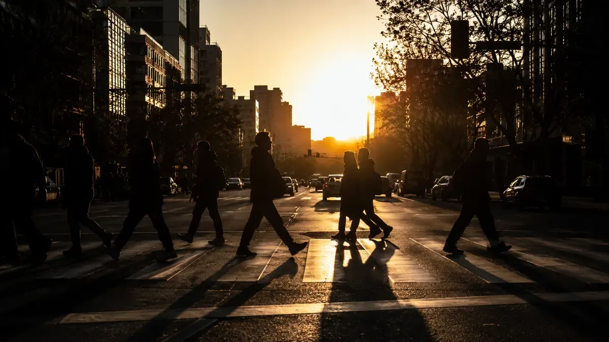 Siluetas de peatones cruzando una avenida urbana a contraluz al atardecer
