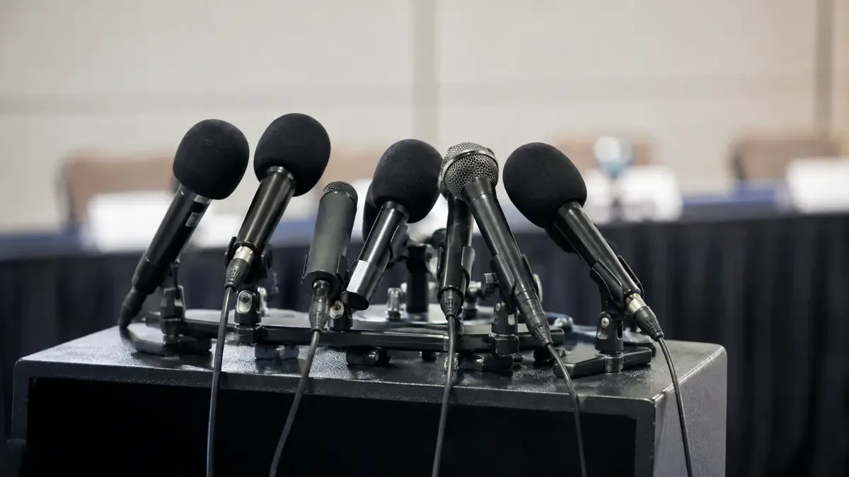 Microfonos sin marca agrupados sobre un atril vacio en una sala de conferencias