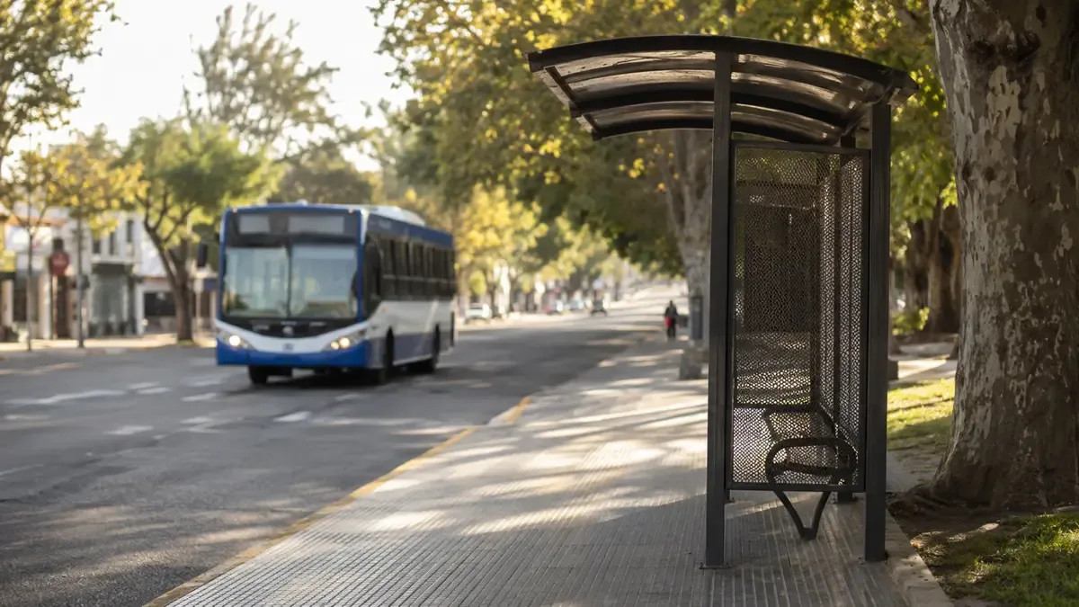 Parada de colectivo con refugio metálico en una avenida del conurbano